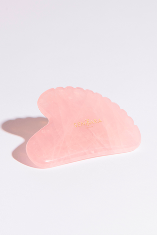 Gua sha en quartz rose de Sentara Holistic avec logo doré, pour le massage facial et le bien-être holistique.